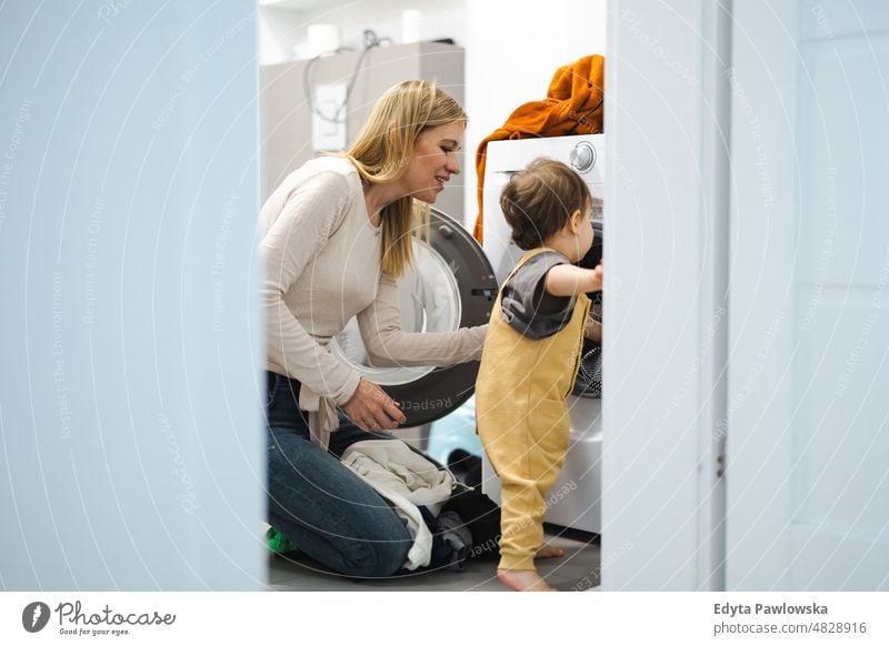 Mother doing the laundry together with her young child adult affection baby bonding boy candid care childhood domestic enjoying family fun happiness happy home