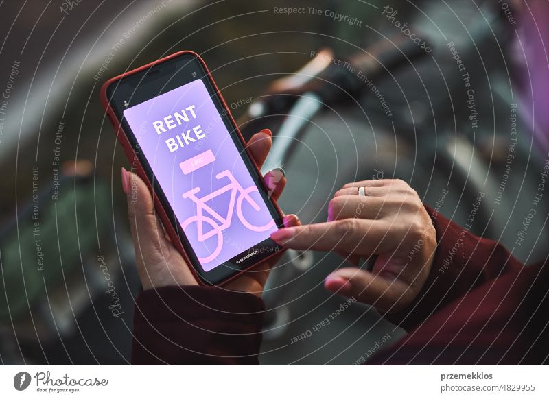 Woman renting bike using rental app on mobile phone. Using bike sharing city service. Paid rent of electric scooter. Using smartphone to rent and pay for public eco transport