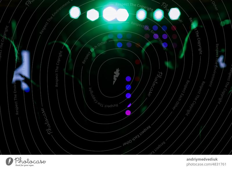 cheering crowd in front of bright blue green stage lights. Silhouette image of people dance in disco night club or concert at a music festival. applauding