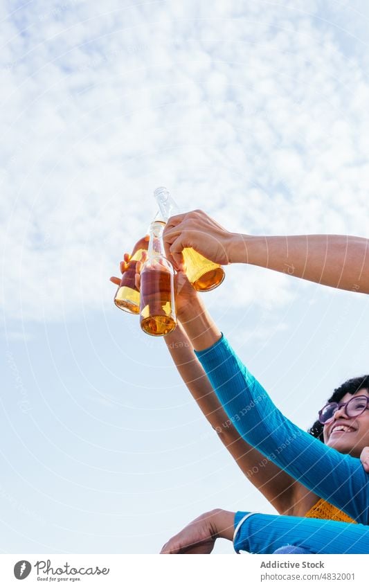 Unrecognizable friends proposing toast underneath blue sky beach sea beer bottle arm raised hands weekend summer man women crop rest vacation resort water