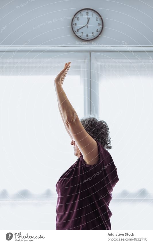 Senior woman exercising in morning exercise stretch home gymnastic arm raised training early fitness female elderly senior aged sunlit healthy lifestyle