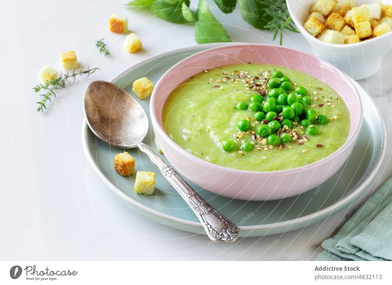 Healthy cream pea soup in a bowl green vegetable vegetarian puree healthy light diet bread cubes spoon garnish herb aromatic delicious recipe dinner lunch thyme