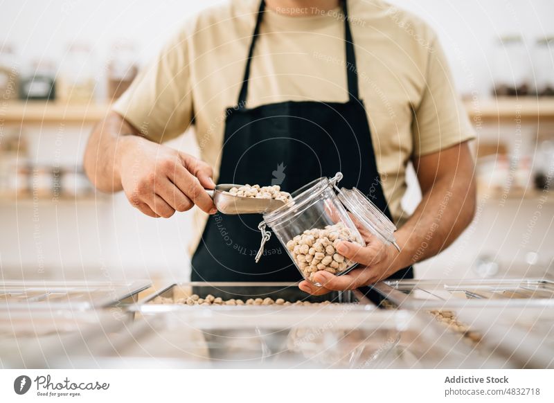 Shopkeeper filling glass jar with chickpeas shopkeeper anonymous store dry pour local seasoning customer ecological scoop consume buyer purchase female shovel