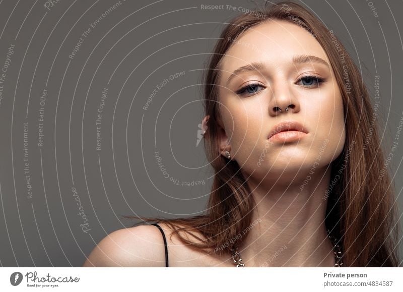 Portrait of a beautiful young woman with clean fresh skin, dark long hair, beautiful lips, natural make-up, looking at the camera, on a gray studio background with copy space