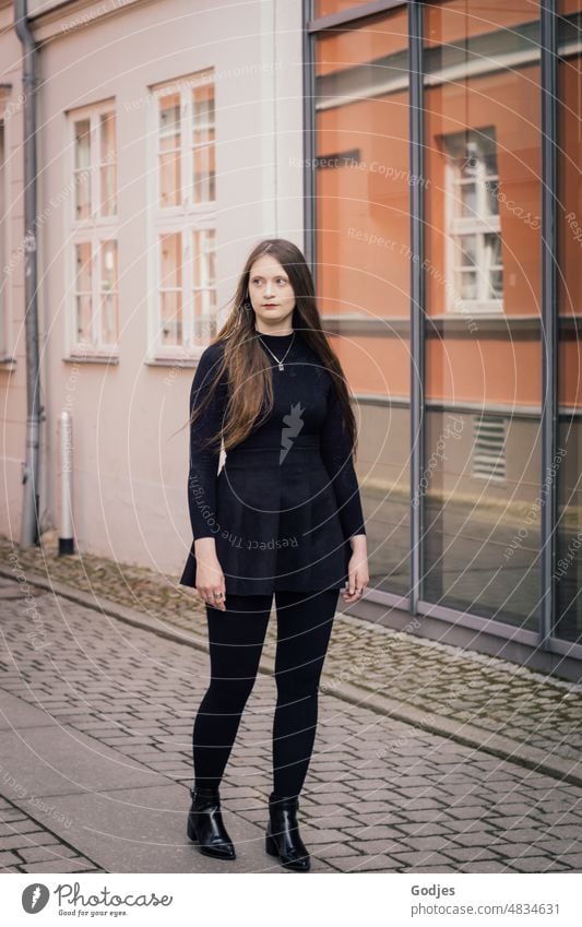 Young woman walking along a path in front of mirrored facade portrait Woman Looking Long-haired Feminine Face Meditative feminine Skeptical look Dress Intensive