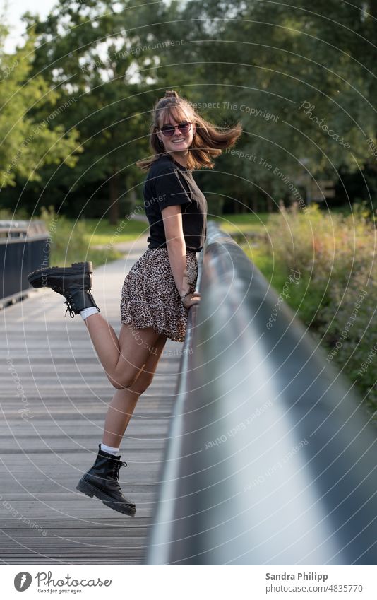 Young woman on bridge smiling at camera Bridge railing Boots Skirt stylish Long-haired Sunglasses Feminine Exterior shot pretty Full-length Fashion Brunette