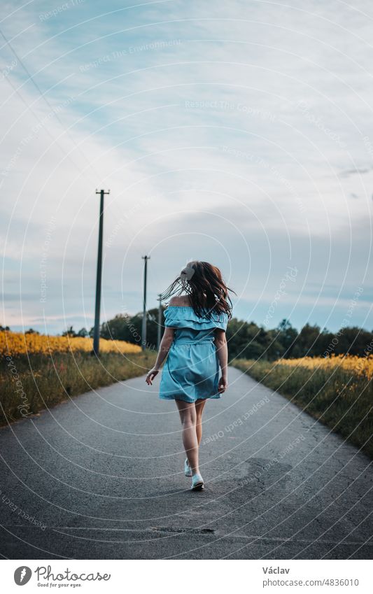 Young 20-24 year old slim brunette in a light blue summer dress dances on the road to the rhythm of the music. Candid portrait of a real ordinary person enjoying movement and dancing. Knowing oneself