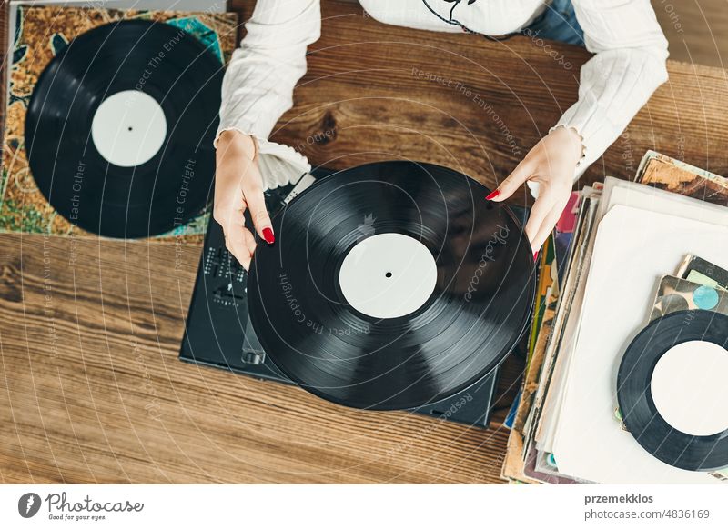 Young woman listening to music from vinyl record player. Playing music on turntable player. Female enjoying music from old record collection at home analog