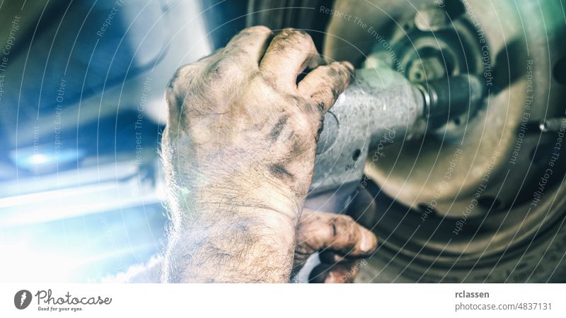 Mechanic changing a car tire in a workshop on a vehicle on a hoist using an electric drill to loosen the bolts in a concept of service or replacement mechanic