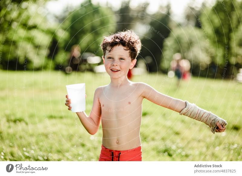 Happy boy with glass water summer shirtless splash cheerful happy bucket childhood positive lawn garden joy smile holiday nature carefree enjoy male outdoors