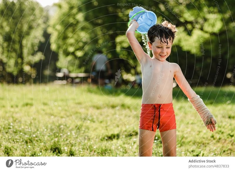 Happy boy playing with water shirtless childhood summer park kid lawn happy nature activity athlete carefree naked torso little cheerful meadow together sun