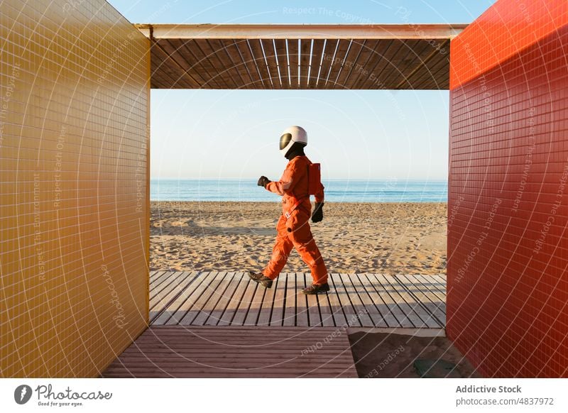 Unrecognizable spaceman walking on alien beach astronaut sea admire building architecture futuristic concept explore spacesuit sand geometry blue sky cosmonaut