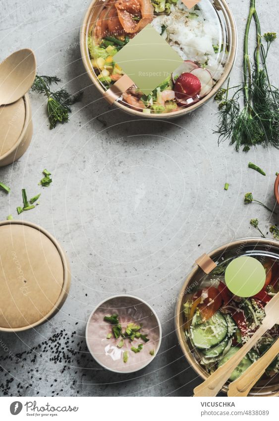 Healthy salads lunch in sustainable packaging with empty label mock up at grey table background with herbs and biodegradable food containers. Delicious to go poke bowls.