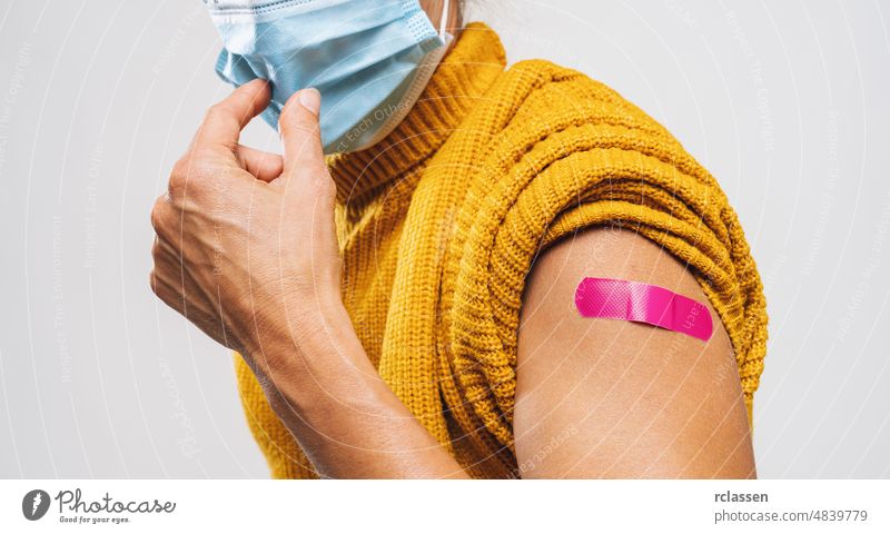 Vaccinated Woman Showing Arm With Pnk Plaster Bandage Protection would like to takes off Face Mask, After Covid-19 Vaccine Injection Posing Gray Background, Coronavirus Vaccination, copy space