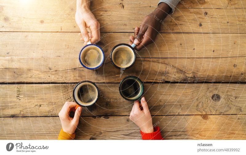 Friends group drinking coffee in a bar restaurant - People hands cheering and toasting on top view point - Social gathering concept with white and black men and women together