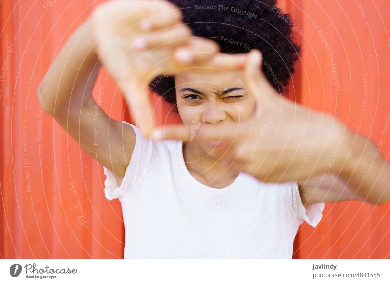 Cheerful African American woman shows a frame from hands like photograph. sign eyes face gesture black curly person girl outdoors young hair african american