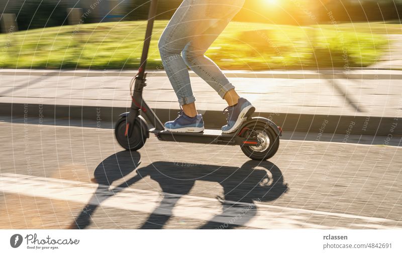 woman riding black electric kick scooter at cityscape at summer, motion blur e-scooter downtown sneakers bike drive activity electrically fun lifestyle future