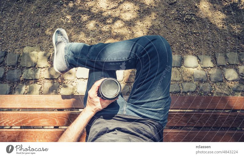 Point of view shot of a man sits on a bench in the park and holding a take away coffee pov hand people lifestyle caucasian healthy beverage close-up plastic go