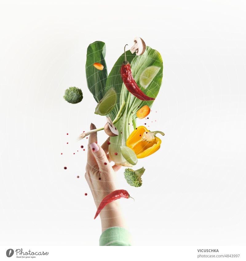 Flying vegetarian food ingredients with women hand at white background. vegetables flying bok choi mushrooms bell pepper chili pepper broccoli lime levitating