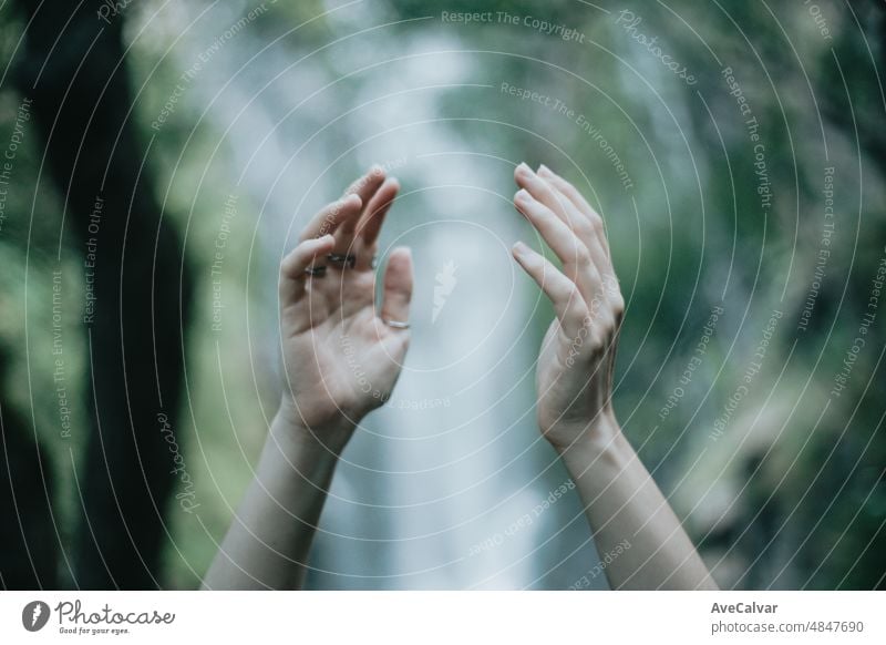 Moody image of an selective pair of hands hands in front of a waterfall during a sunny day, peaceful scenario, copy space. help and self help concept,mental health concept.Therapy and looking for help