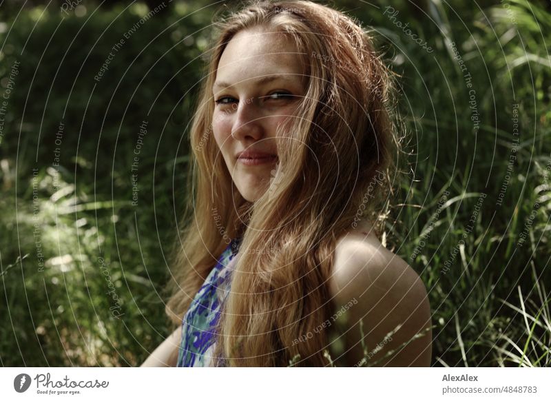 Young red blonde long haired woman sitting in tall grass looking sideways at camera smiling Woman youthful pretty Slim Grass Nature Blonde cheerful fortunate