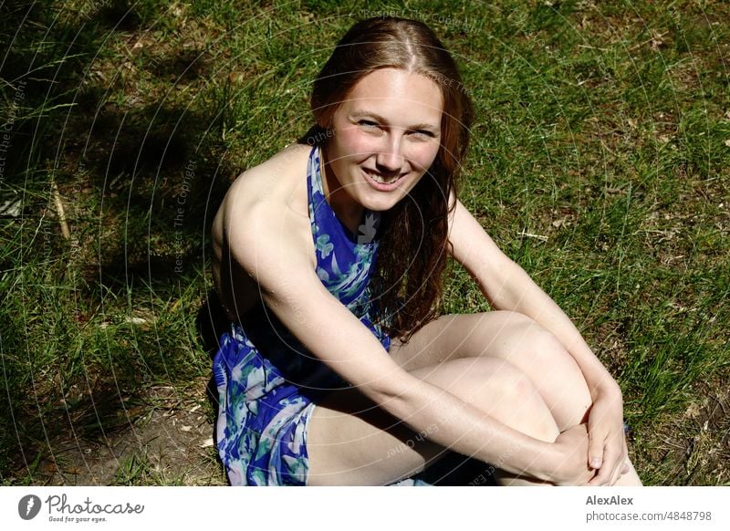 Young red blonde long haired woman with wet hair sits in grass and looks sideways at camera smiling Woman youthful pretty Slim Grass Nature Blonde cheerful