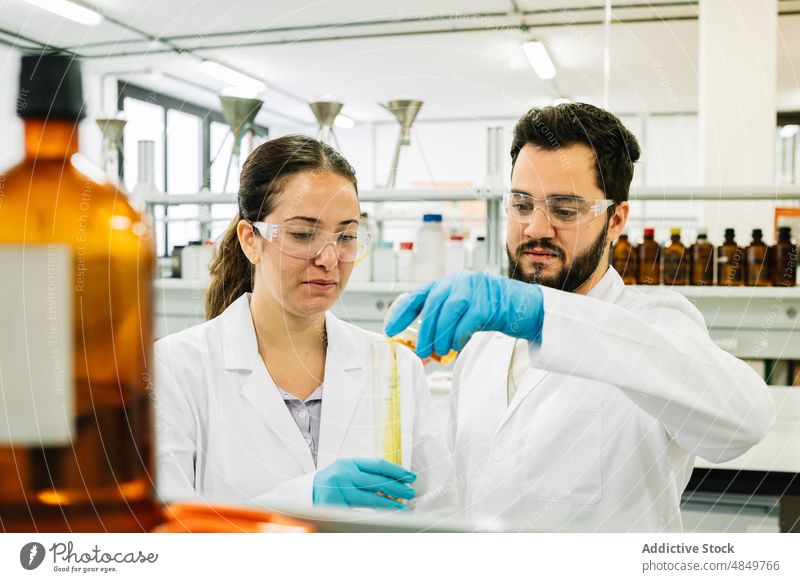 Scientists pouring chemical liquid into test tube scientist coworker laboratory chemist colleague experiment sample research reagent science focus beaker flask