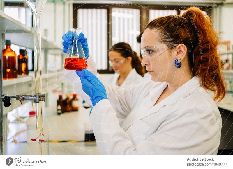 Serious chemist examining liquid in flask in lab woman scientist examine laboratory scientific chemical experiment sample test research expertise science focus