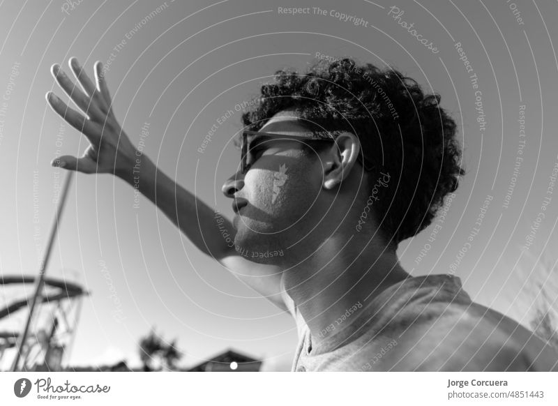 young latin guy in an amusement park, looking at the sun and covering his hand causing shadows on his face. portrait person casual lifestyle leisure joy