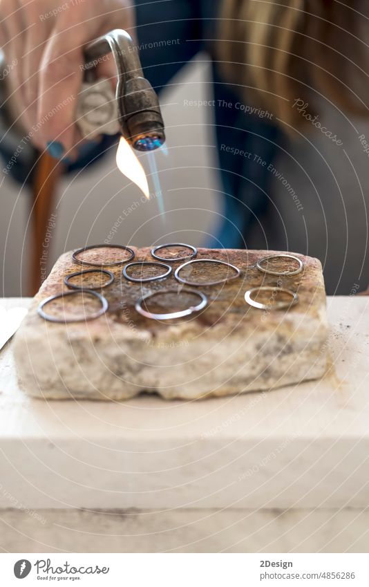 close-up of jeweler's hands working with a blowtorch on a piece of silver jewelry in his workshop. craftsman fire flame manufacturing tool entrepreneur