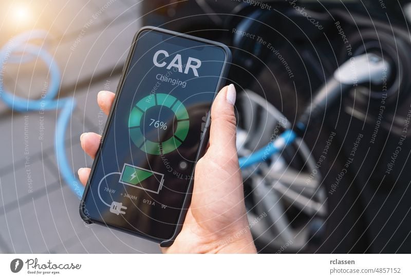 Woman Charging Electric car with Cable Looking at App On Mobile Phone. Close up of smartphone screen. Hand holding smart device. Mobile application for eco transportation.