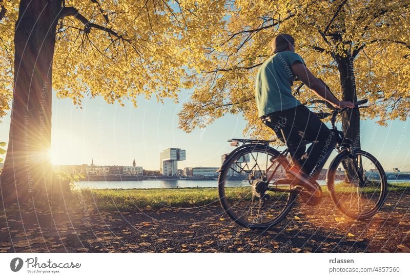 young man ride a bicycle at the rhine shore in cologne, germany crane houses eve city dom rheinauhafen architecture cologne cathedral sun clouds sky sunbeams