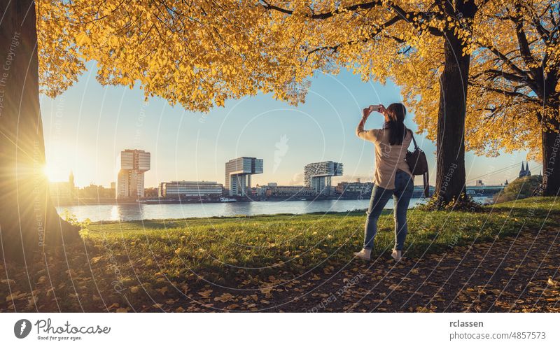 Woman takes a picture from the Skyline of Cologne at autumn cologne crane houses eve city dom rheinauhafen architecture cologne cathedral shore sun clouds sky