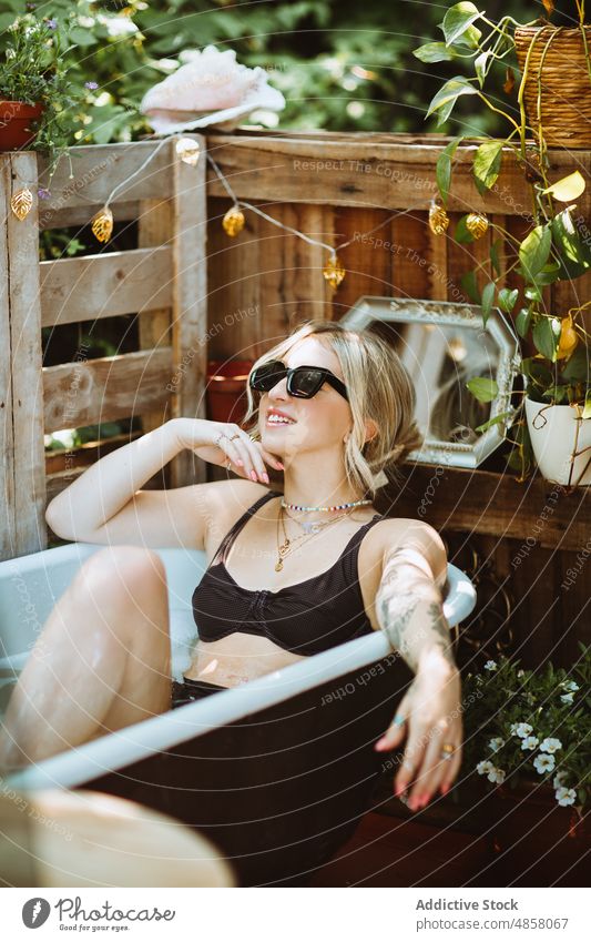 Woman in bath on patio woman bathtub water skin care terrace wellbeing chill routine style sunglasses appearance feminine rest summer charming lady summertime