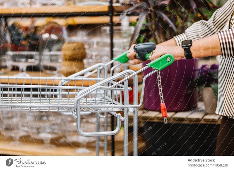 Crop customer with cart walking near shelves woman trolley shop push shelf commerce visit retail female elderly senior aged store plant potted glassware