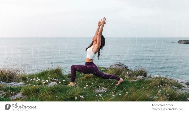 Athletic lady standing in Virabhadrasana pose while practicing yoga at seaside woman warrior pose virabhadrasana stretch mindfulness flexible wellness cliff