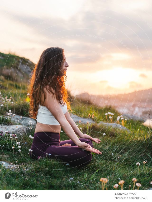 Young woman sitting in Lotus pose and meditating in nature lotus pose meditate athlete activewear hill padmasana practice yoga mudra female sportswear grassy