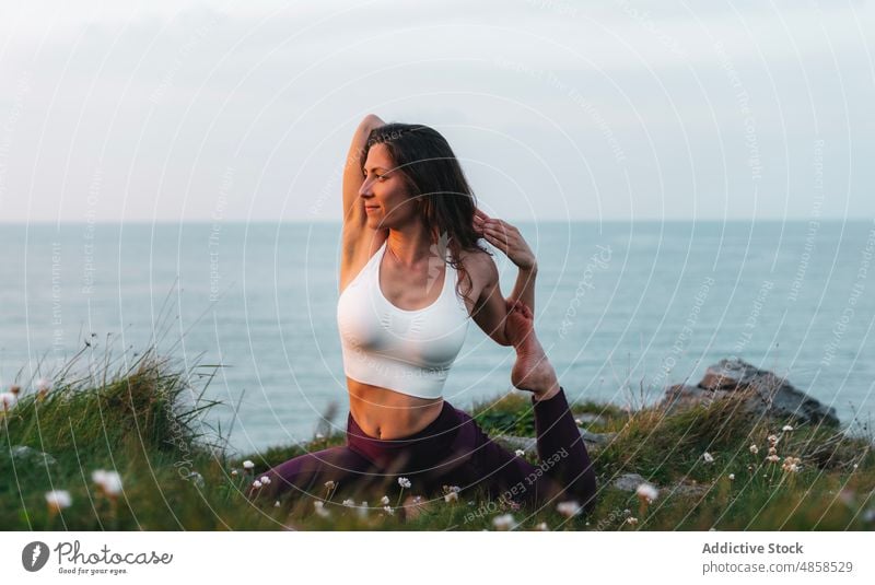 Fit woman doing yoga on seashore athlete sportswear grassy eka pada raja kapotasana practice nature healthy lifestyle hill ocean water seaside mermaid pose