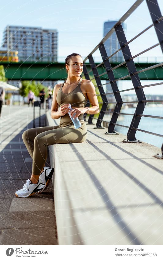 Pretty young woman with earphones takes a break after running in urban area athlete athletic arabic exercise female fit fitness bottle drink healthy jogger