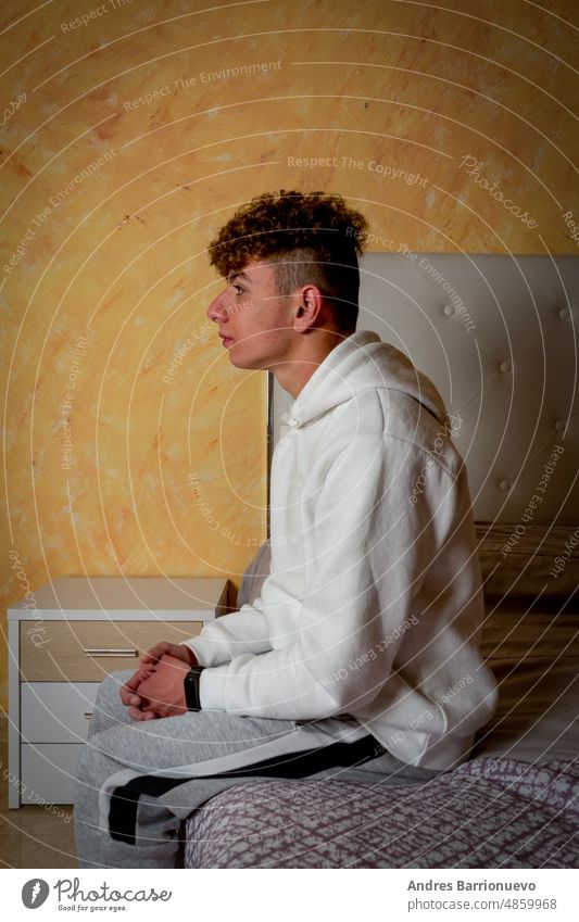 Young man with curly hair sitting on the bed in his room with sad and depressive attitude, loneliness concept. bedroom young stressed sadness depression