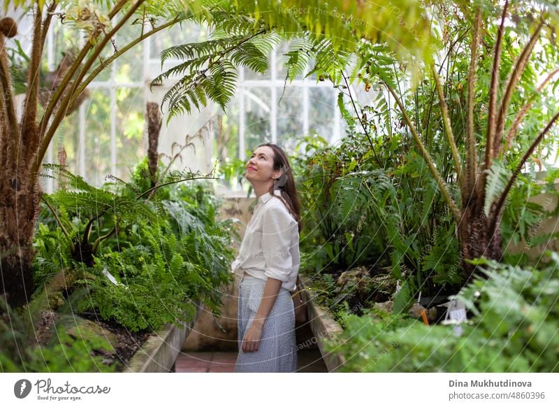 Young woman at greenhouse with tropical plants traveling and admiring beauty of nature. Female tourist visiting botanical garden, studying plants.