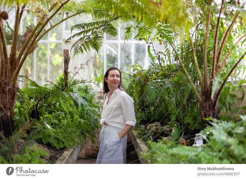 Young woman at greenhouse with tropical plants traveling and admiring beauty of nature. Female tourist visiting botanical garden, studying plants.