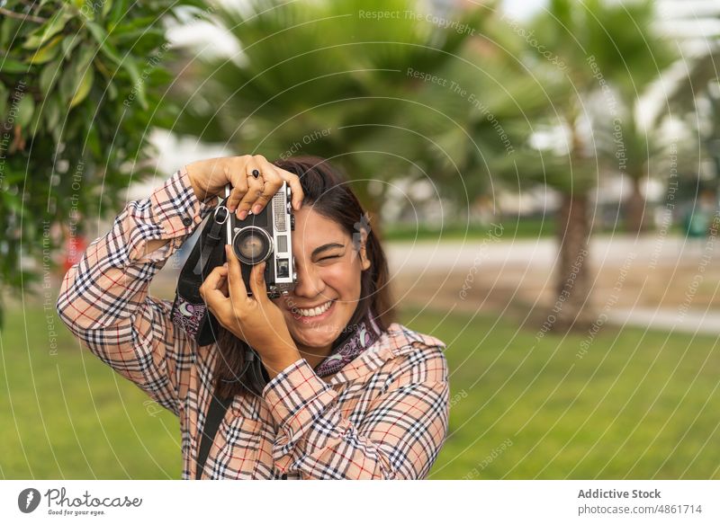 Positive ethnic woman photographing on retro camera in city park take photo photo camera vintage tourist smile cheerful photography tropical happy nature