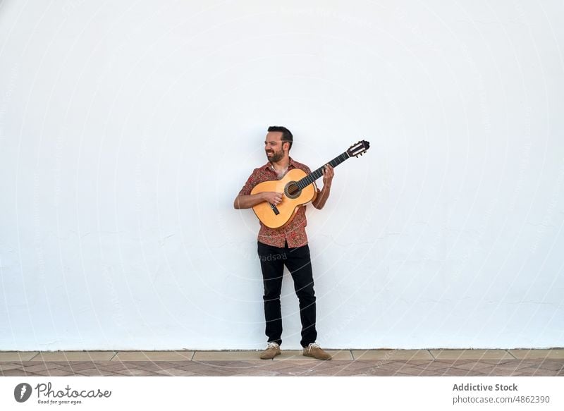 Cheerful man playing acoustic guitar musician smile guitarist street song hobby wall instrument happy sound perform skill entertain positive content glad