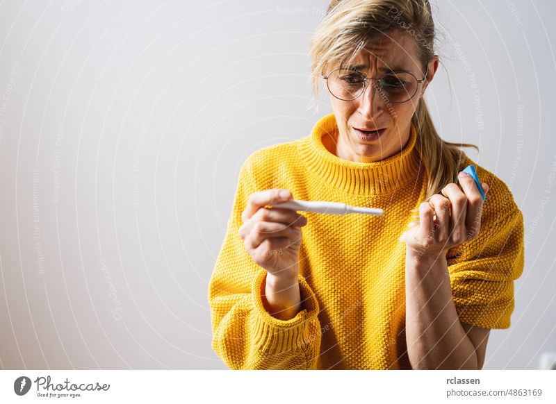 young attractive woman with glasses holding pregnancy test at home looking at positive result in shock and stress having surprise in girl unwanted maternity concept image