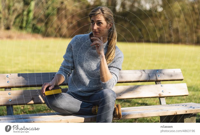 thoughtful woman sitting in the park on at a bench. student thinking with a book in the park concept image girl hair pretty tree attractive flirt watch