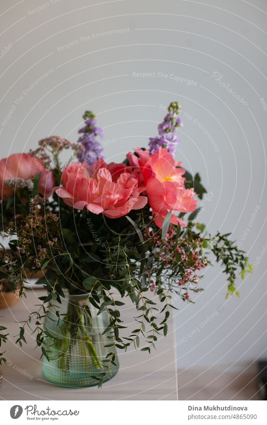 Beautiful bouquet with pink coral peonies and greens in a vase on wooden table at home. Home decor with flowers. Decorating home and coziness. Gift for a birthday, anniversary or Mother's Day. Romantic gesture.