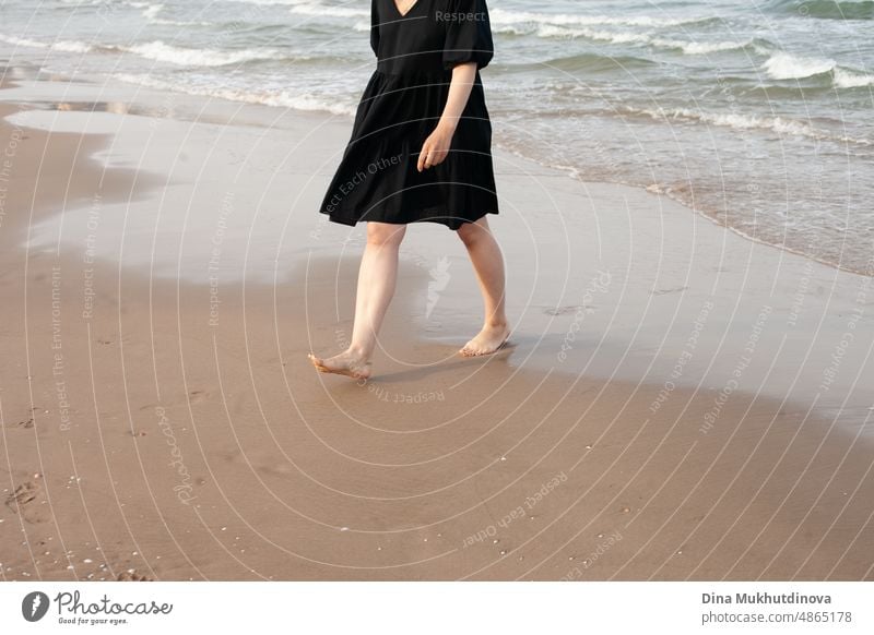 Barefoot woman walking on the sandy beach away from the sea waves. female tourist on vacation and traveling. Barefoot feet on sand. Waves of sea along the shore. Woman walking along the coast.