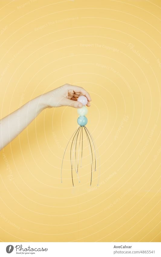 Hand holding an head massage tool over a yellow background with copy space. Relax and chill funny concept image. Young people relaxing after work relaxation