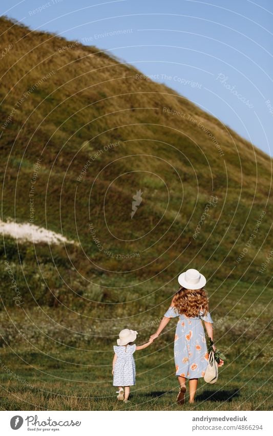 Young mother walking with her little daughter in the green field. Family holiday in garden. Portrait mom with child together on nature. Mum, little daughter outdoors. Happy Mothers Day. Close up.